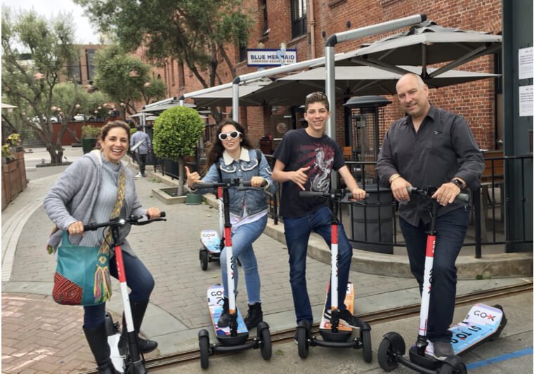 Guests riding Go X scooters outside a restaurant patio